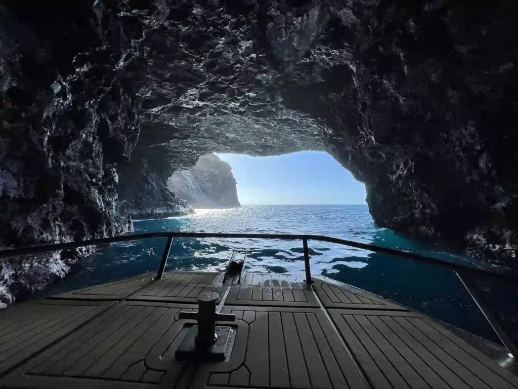 The view from inside a dramatic Na Pali Coast sea cave looking out through the cave opening toward the bright blue ocean and rugged coastline beyond on a Kauai sea caves tour, Hawaii.