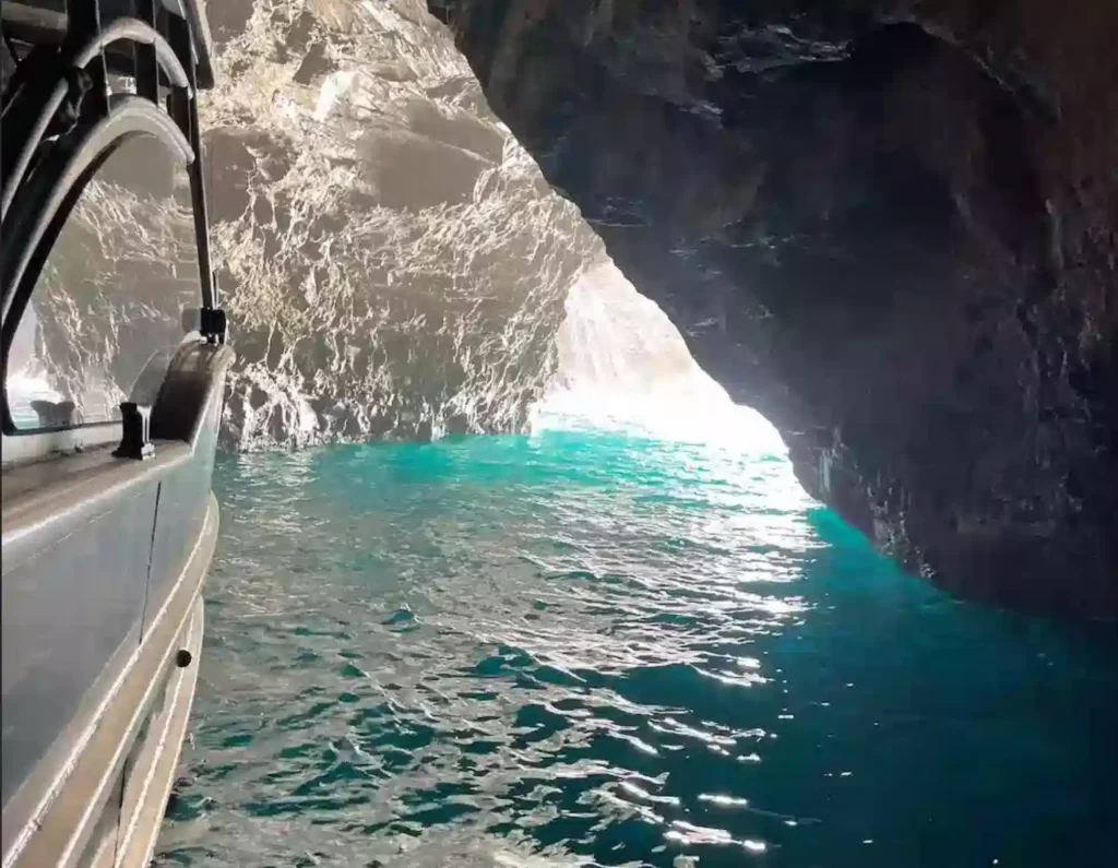 A Makana Charters tour boat entering a glowing Kauai sea cave with vivid turquoise water and dramatic volcanic rock walls on a Kauai sea caves tour, Na Pali Coast, Hawaii.