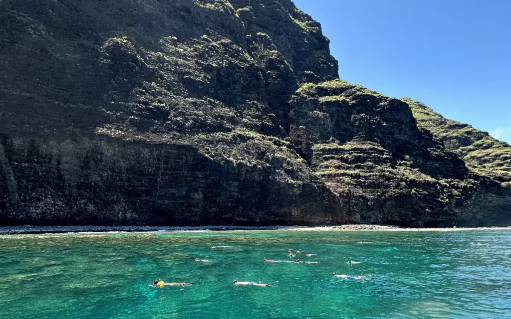 Group of snorkelers in clear turquoise water along the Na Pali Coast cliffs on a Makana Charters Kauai tour