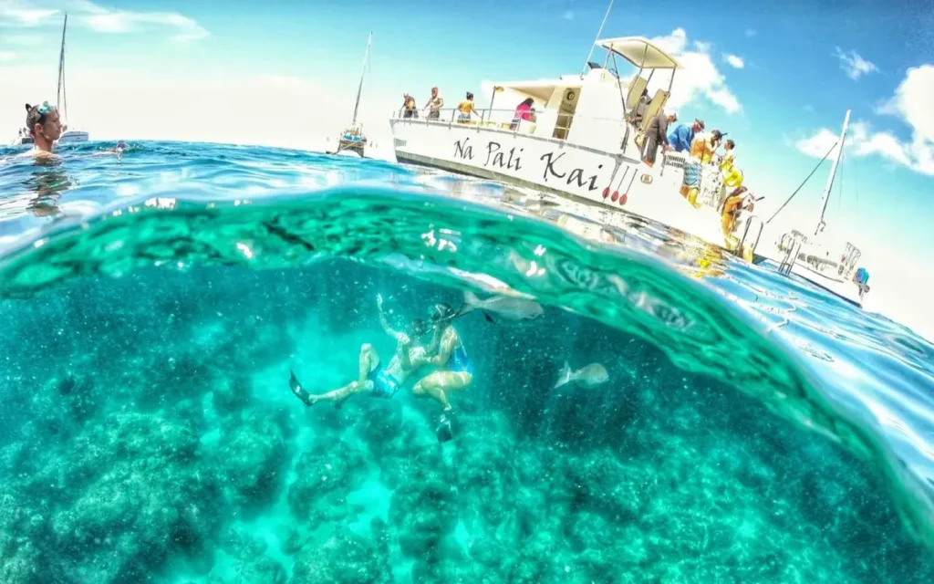 Snorkelers exploring a clear reef on a Makana Charters Kauai snorkel tour beneath the Na Pali Kai boat