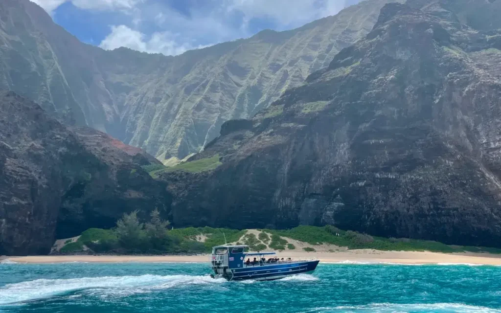 Makana Charters boat anchored at a Na Pali Coast beach beneath towering green cliffs on Kauai
