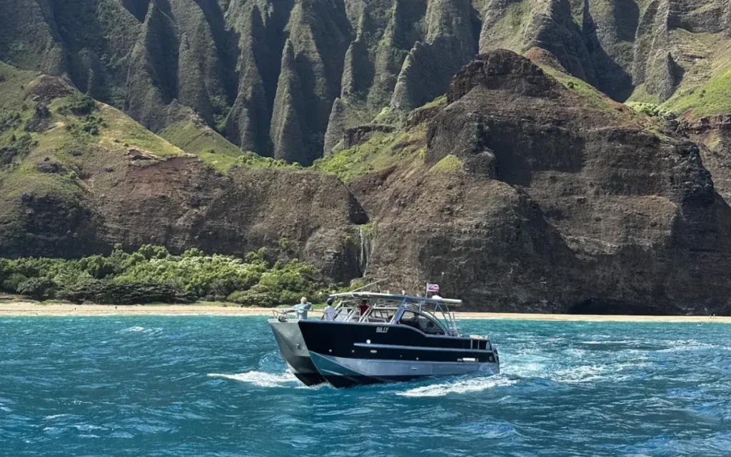 Makana Charters powered catamaran cruising the Na Pali Coast cliffs on a Kauai snorkel tour