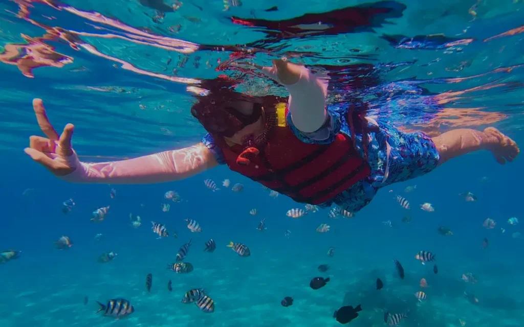 Guest on a Makana Charters Na Pali Coast snorkel tour swimming with reef fish in clear Kauai water