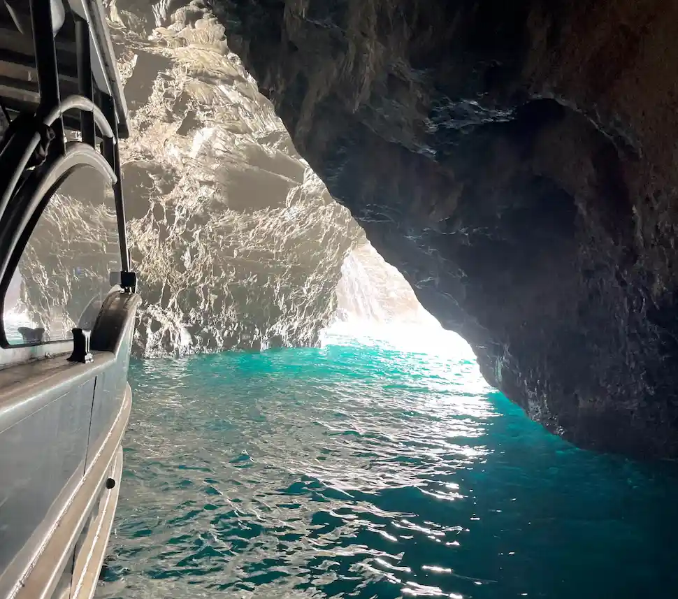A Makana Charters tour boat navigating through a narrow Kauai sea cave passage with dramatic volcanic rock walls and glowing turquoise water on a Kauai sea caves tour, Na Pali Coast, Hawaii.